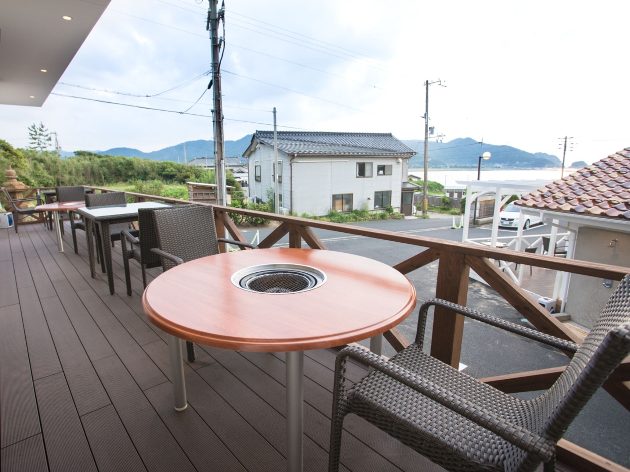 A deck with a round table and wicker chairs, overlooking a residential area and a body of water.
