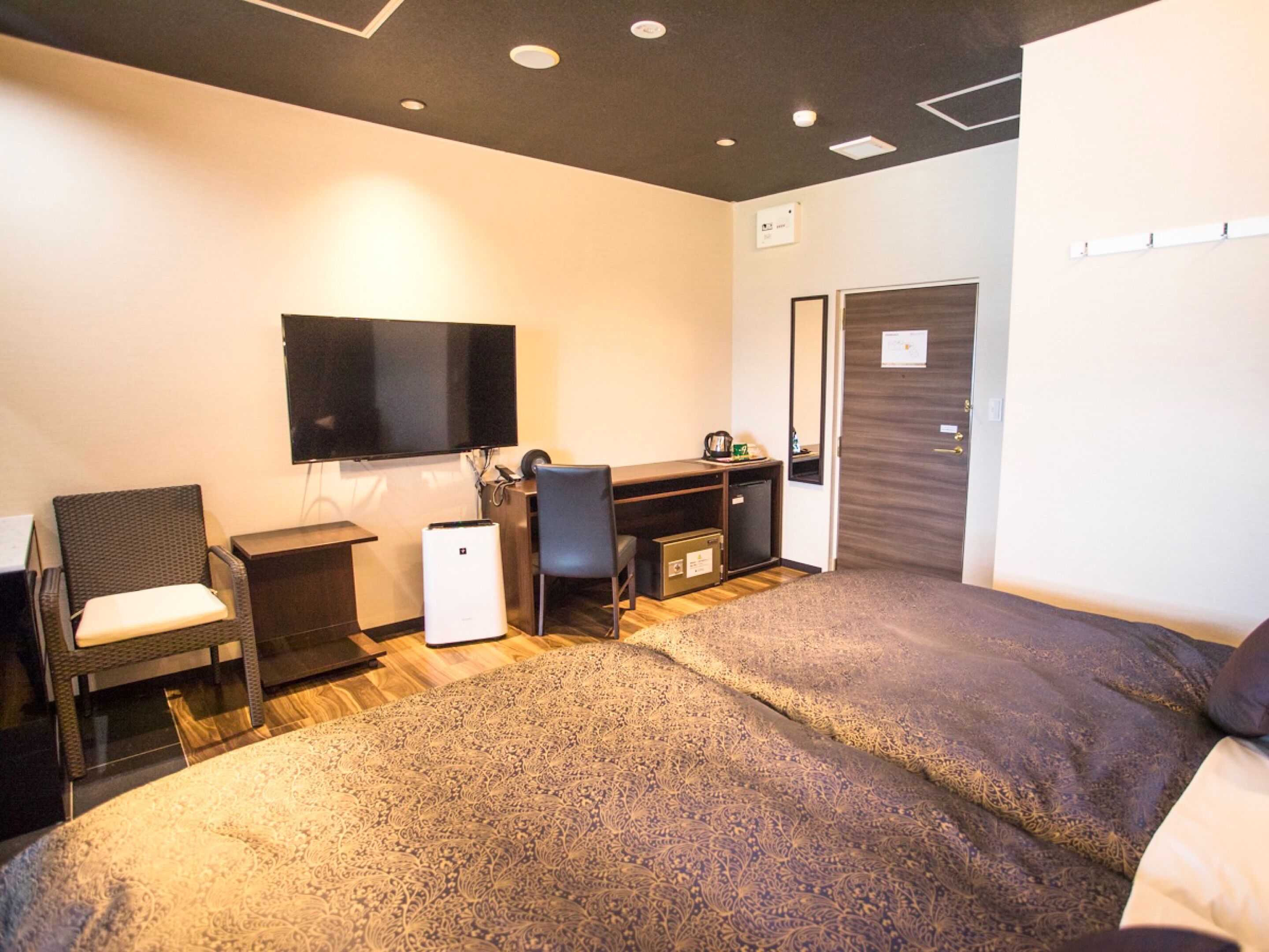 A hotel room with a bed, a desk, a chair, a television, and a wardrobe.