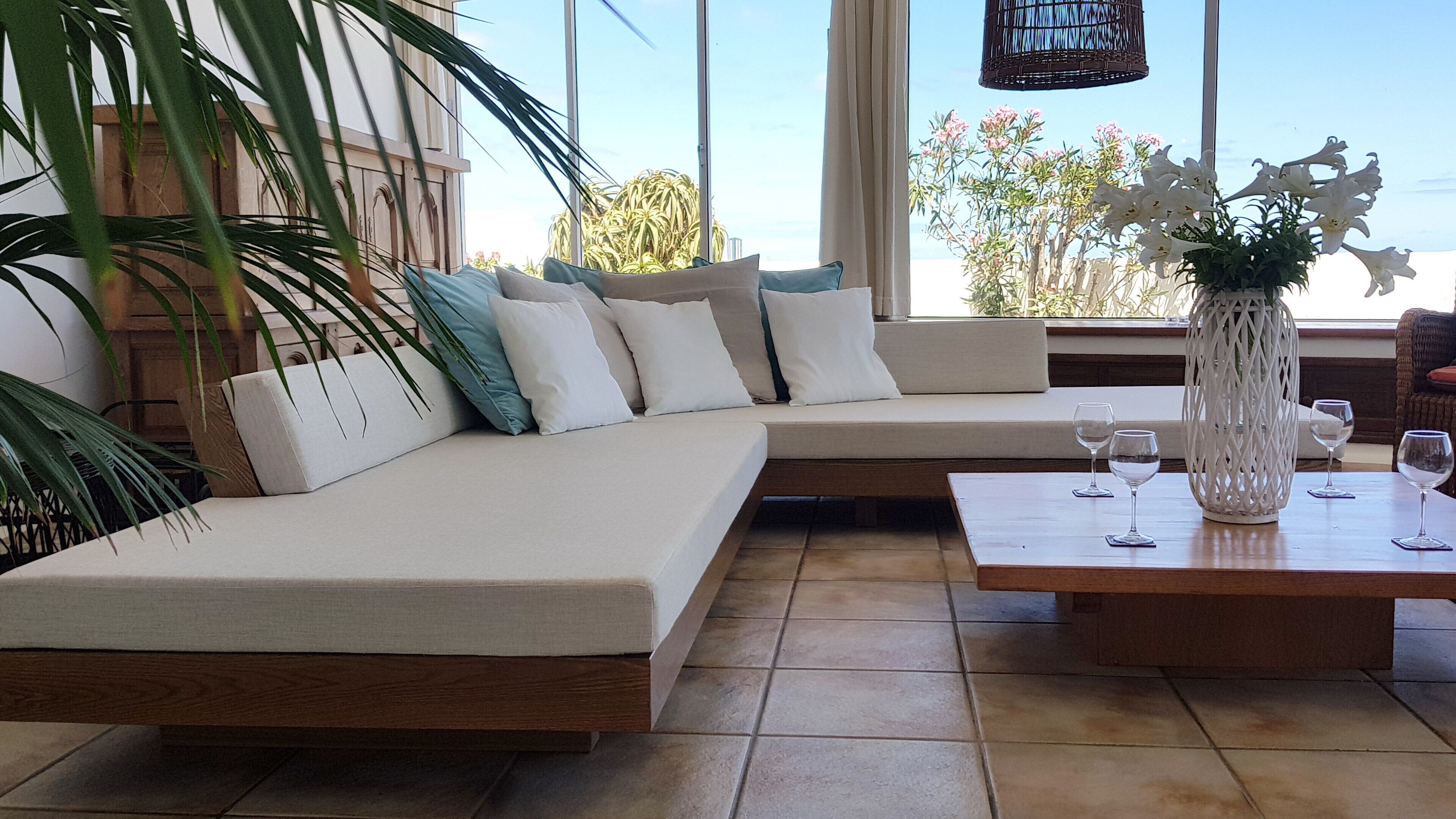 Una sala de estar moderna con un sofá grande en forma de L, una mesa de centro de madera y vista al mar.