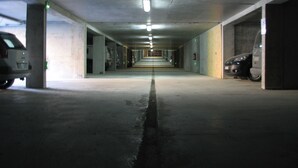 Un parking à plusieurs niveaux, avec des piliers en béton, un éclairage fluorescent et plusieurs véhicules stationnés.
