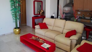 A modern living room with a beige sofa, red cushions, a red coffee table, and a large potted plant. - VistaMar Apartment in Estepona Málaga (Estepona)