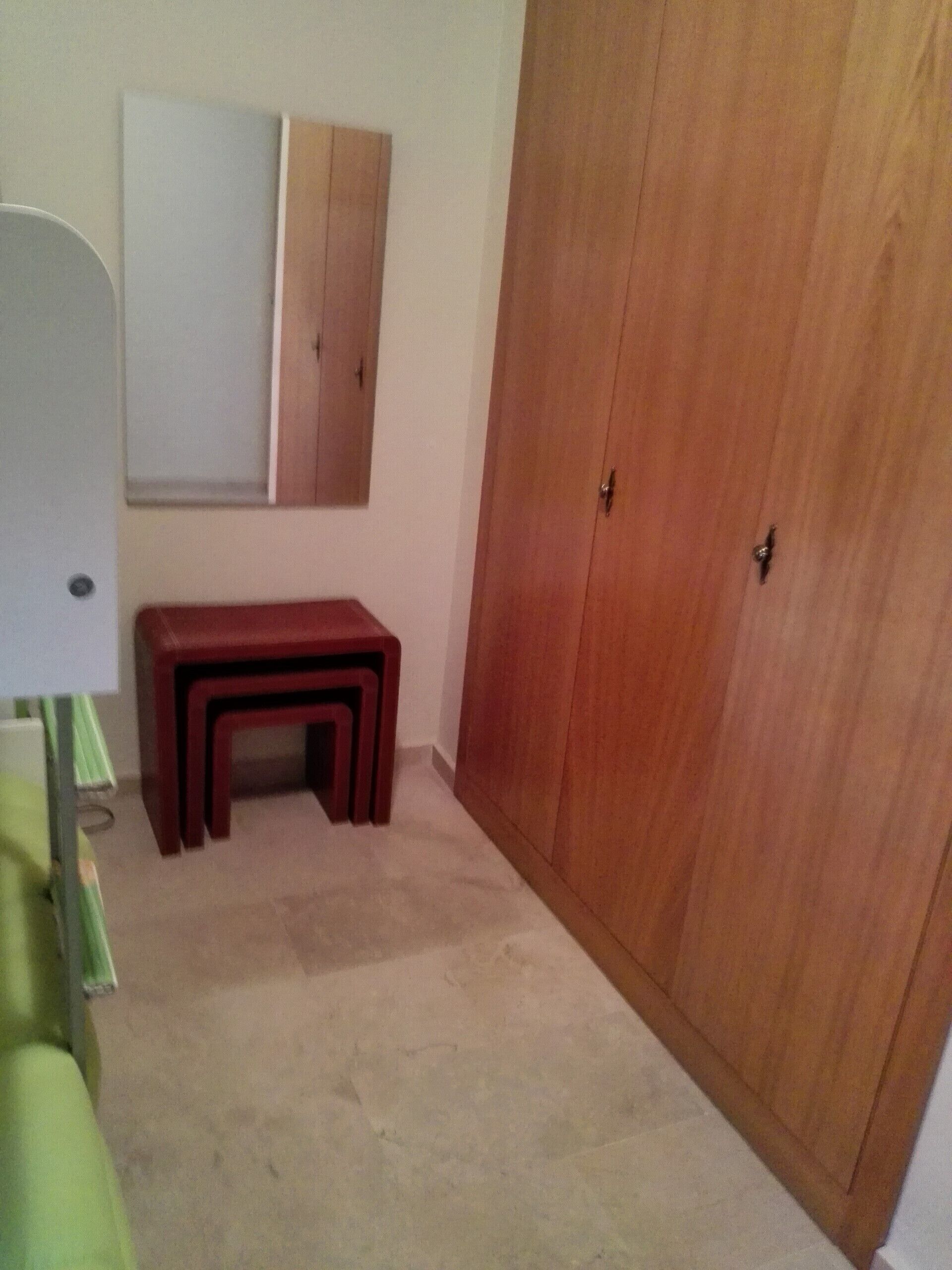 Quarto com guarda-roupa de madeira, um pequeno banco e um espelho na parede.