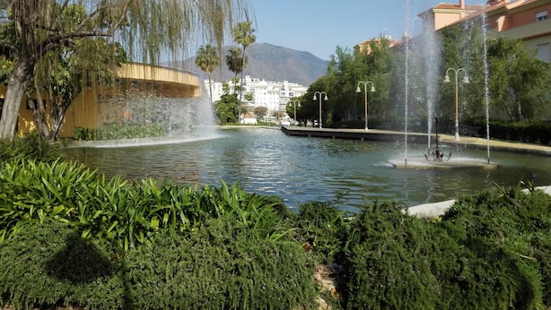 A fountain with water jets in a park with greenery and buildings in the background. - VistaMar Apartment in Estepona Málaga (Estepona)