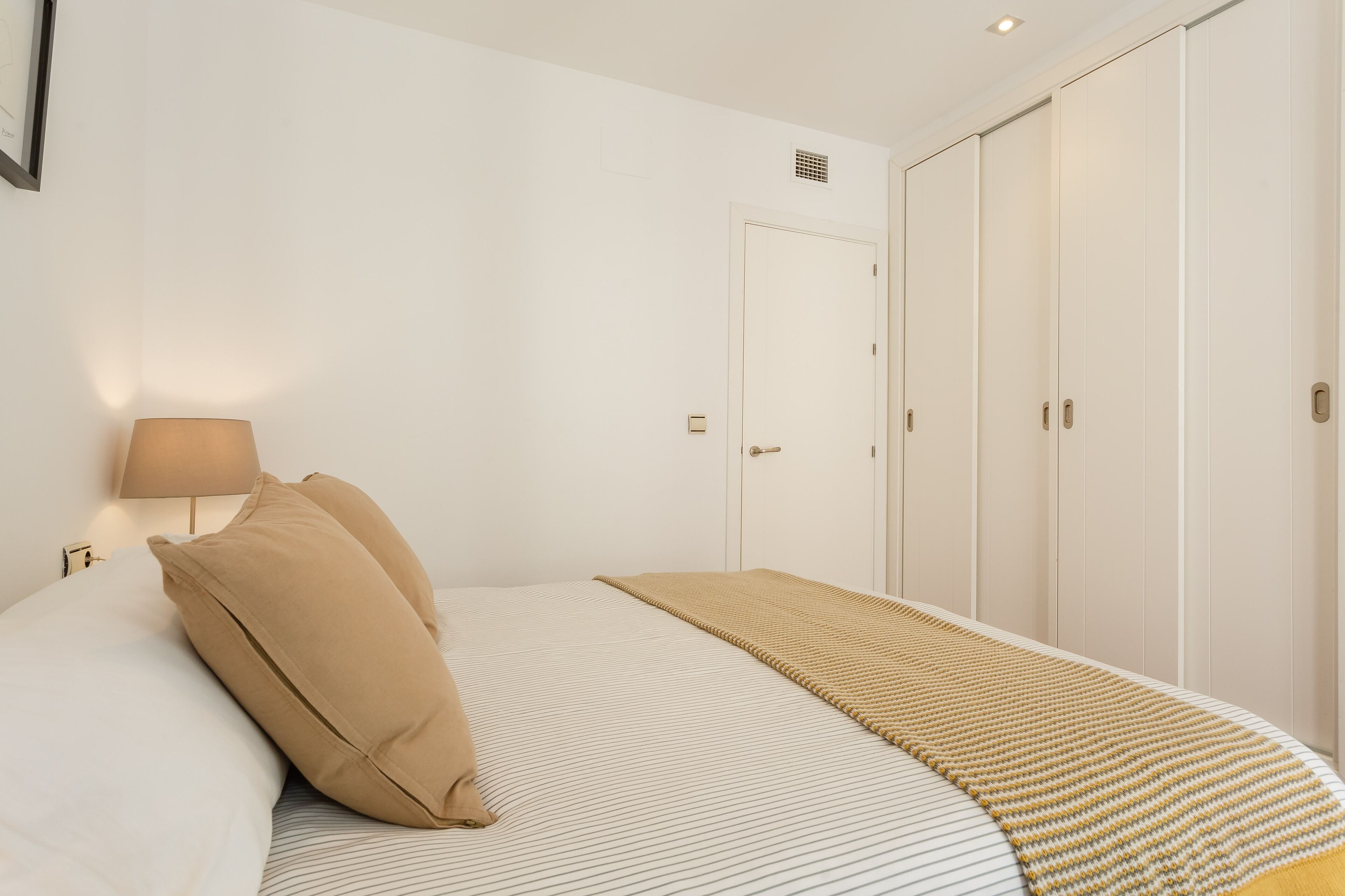 Une chambre à coucher comprenant un lit, une lampe de chevet, une table de chevet, une armoire et une porte.