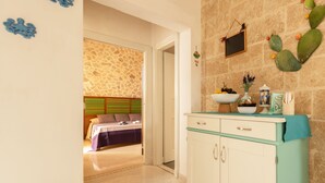 Une pièce avec un mur en pierre, un lit avec une tête de lit verte, une kitchenette avec un plan de travail turquoise et une décoration à thème de cactus.