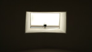 Une pièce avec une petite fenêtre qui projette l’ombre d’une lampe sur le mur.