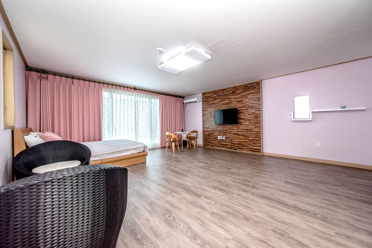 A modern hotel room with a bed, a dining table with chairs, a TV, and a wooden accent wall.