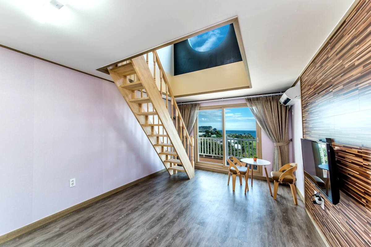 A modern room with a wooden staircase, a balcony with a view, and a flat-screen TV.
