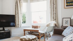 A living room with a television, a sofa, a chair, a table, and a window with curtains.