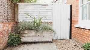 A wooden planter box with plants, a white fence, and a brick wall.