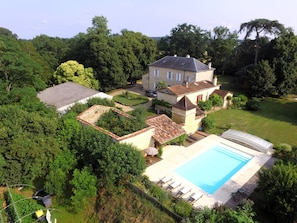 Une grande maison avec une piscine, entourée d’une végétation luxuriante et d’arbres.