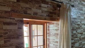 Ein Zimmer mit einer Steinsäule, einem Fenster mit Blick und einer zusammengerollten Decke auf einem Sims.