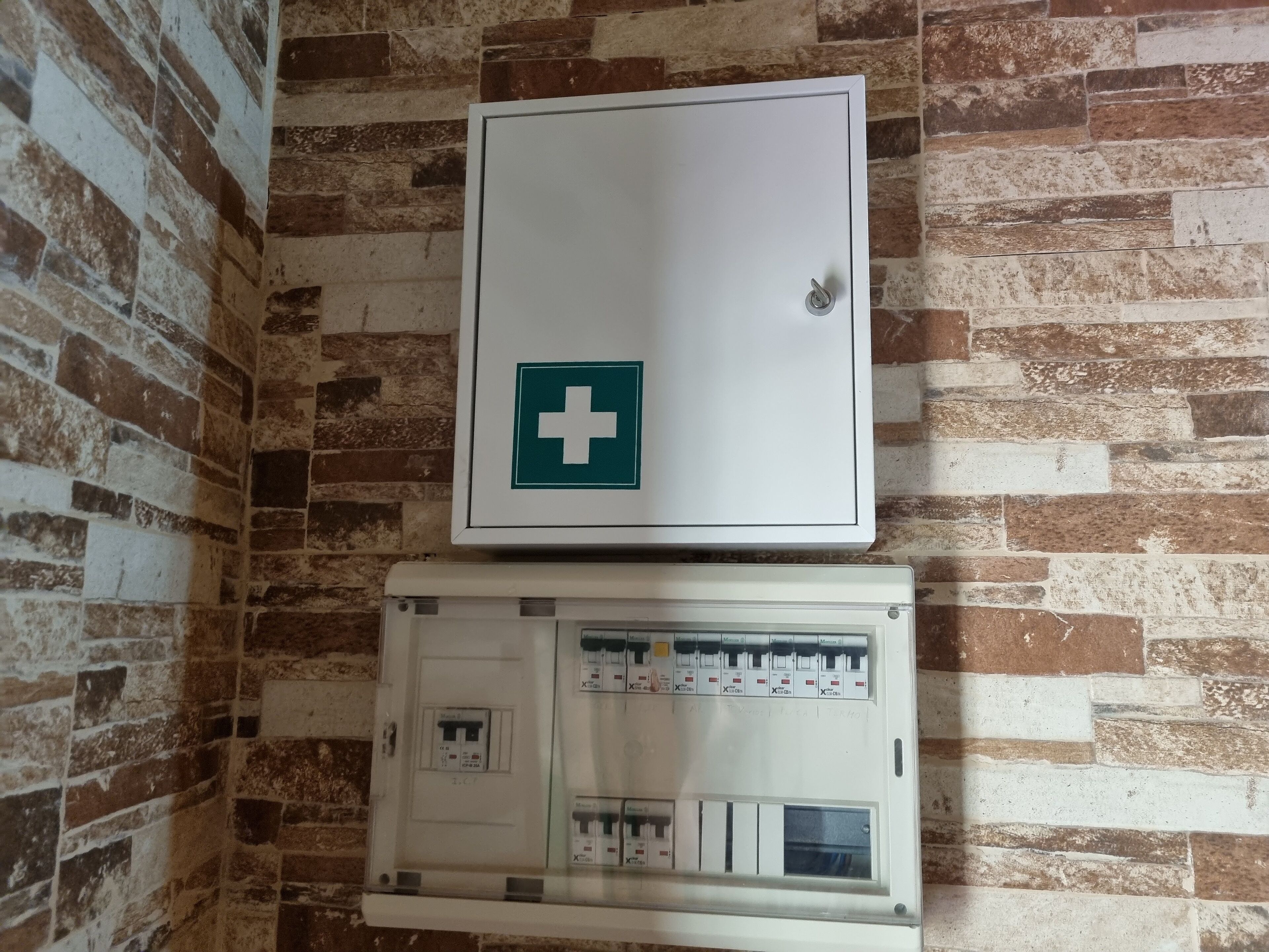 A utility room with a white electrical panel and a white cabinet with a green cross symbol.