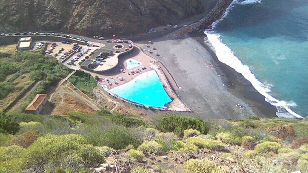 Ein Luftbild eines Küstenresorts mit großem Schwimmbecken, Parkplatz und Strand.