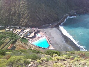 An aerial view of a coastal resort with a large swimming pool, a parking area, and a beach. - Cottage with terrace nestled in a beautiful landscape (Vallehermoso la gomera)