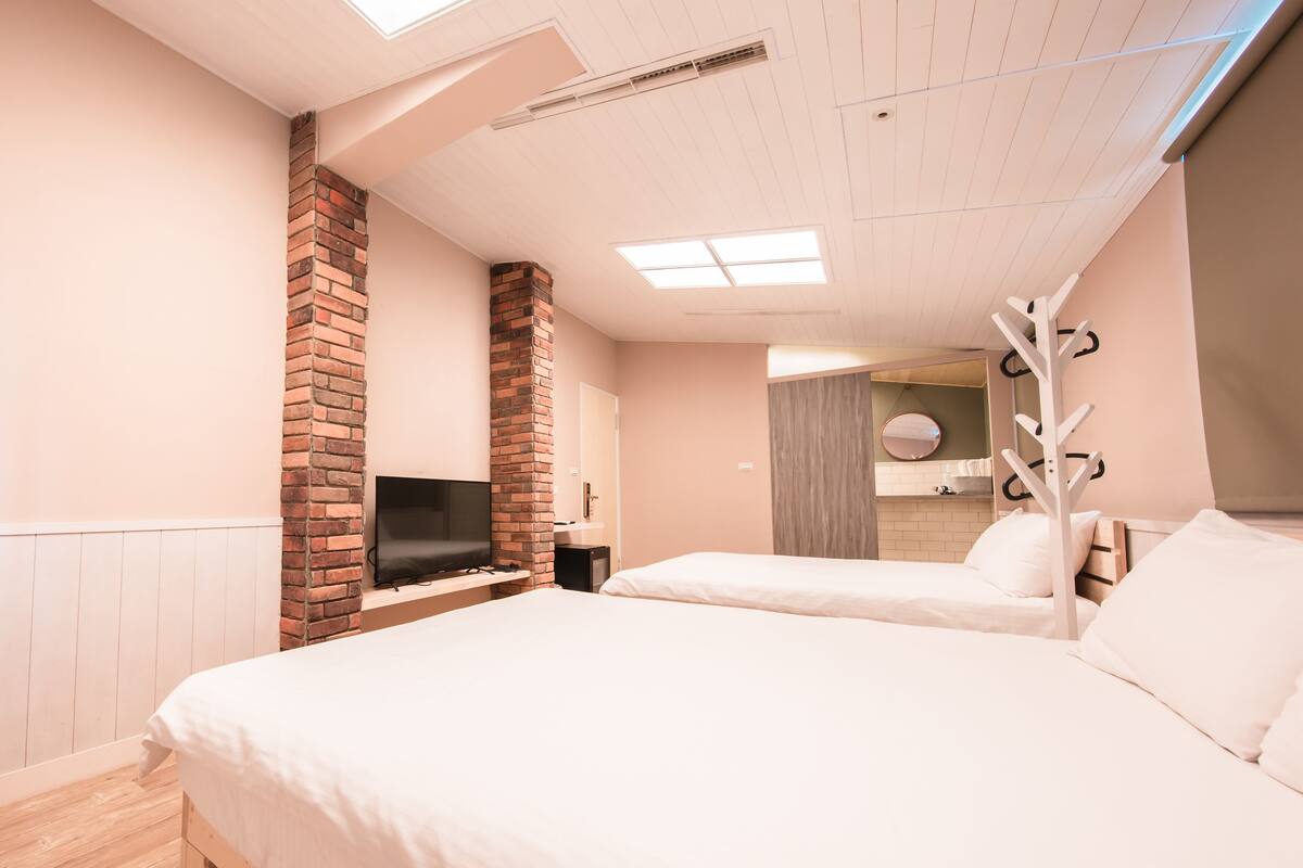 A modern hotel room with a brick fireplace, a flat-screen TV, a wooden bed frame, and a large mirror.