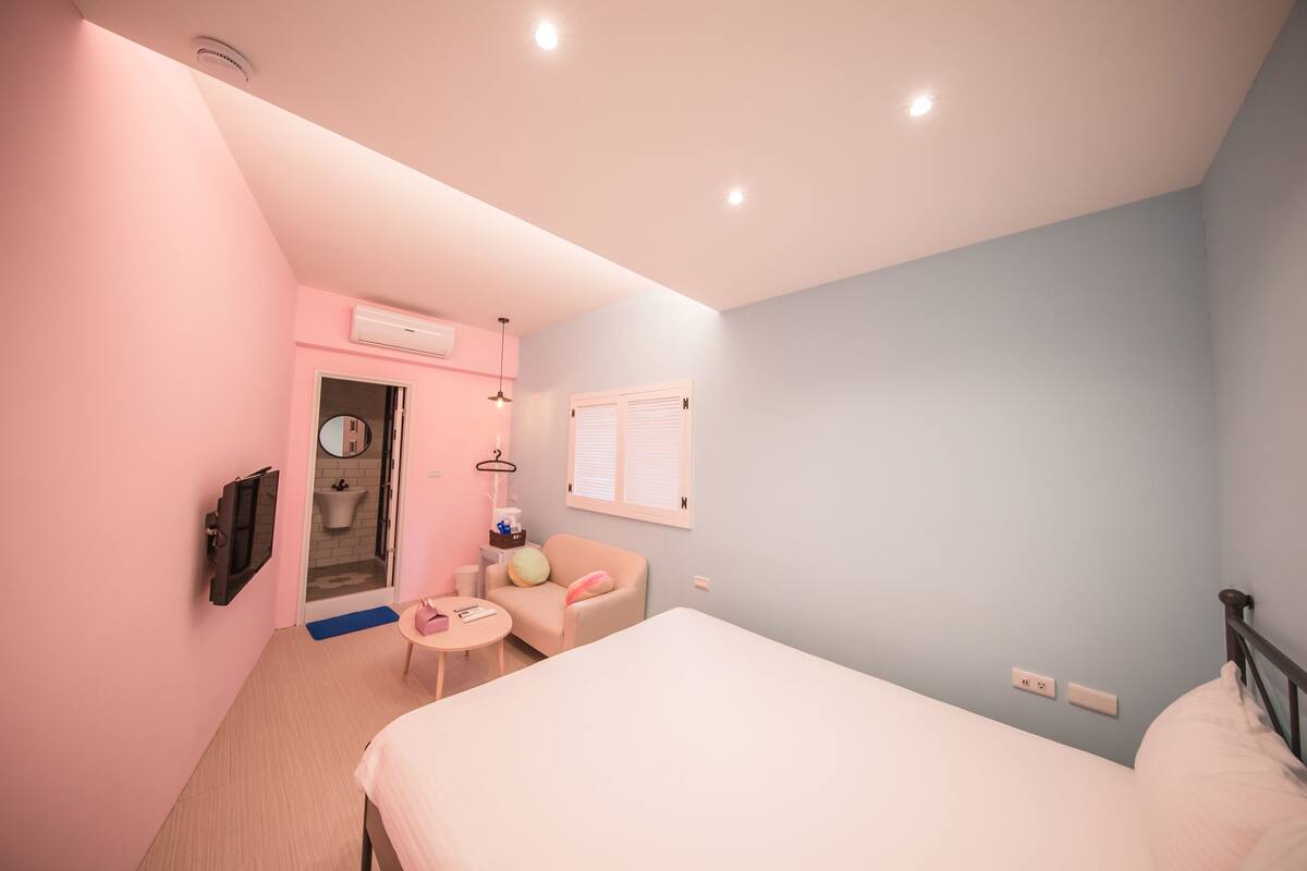 A bedroom with a bed, a chair, a small table, a mirror, and a window.