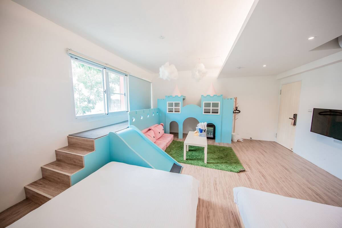 A modern living room with a blue playhouse, a pink sofa, and a staircase.