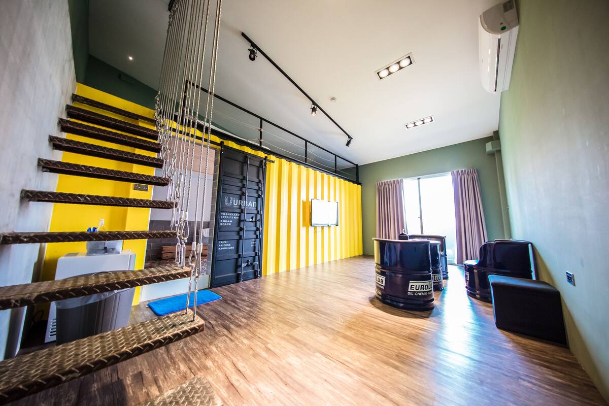 A spacious room with a wooden floor, a yellow and black striped wall, a large window with curtains, and a black chair.