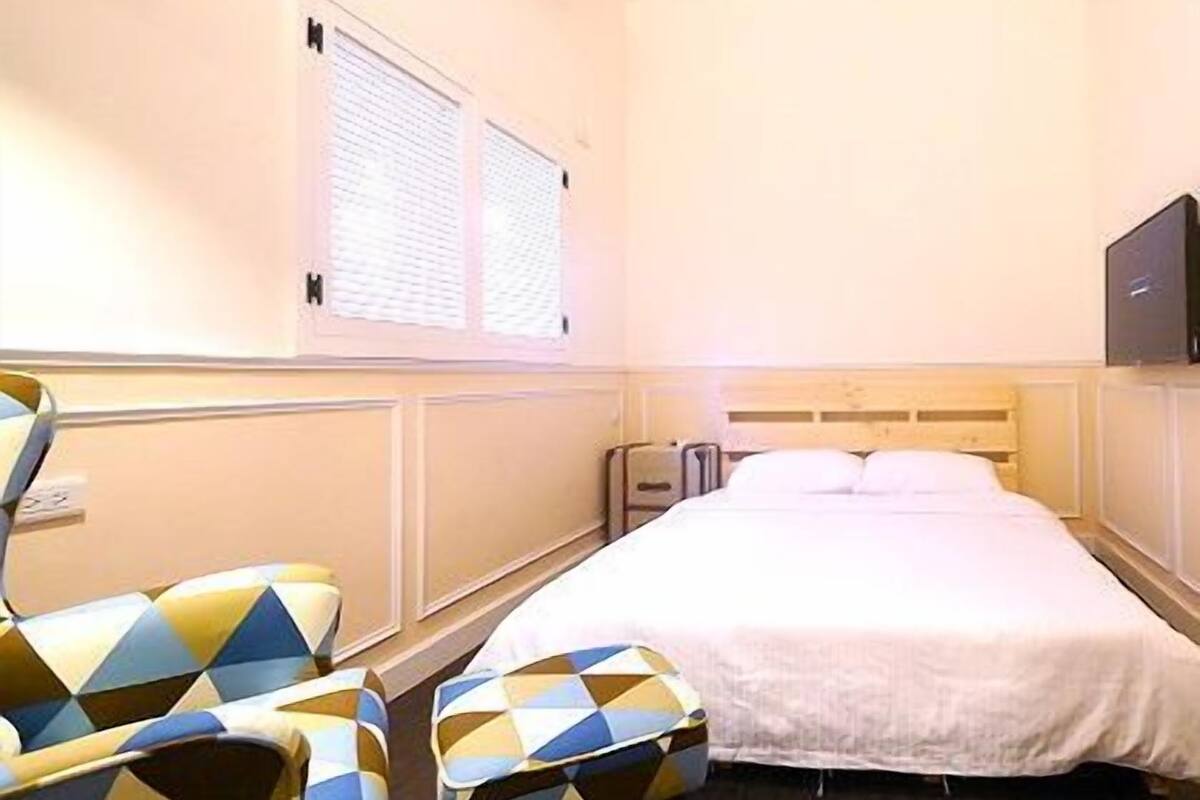 A hotel room with a bed, a chair, a TV, and a window.
