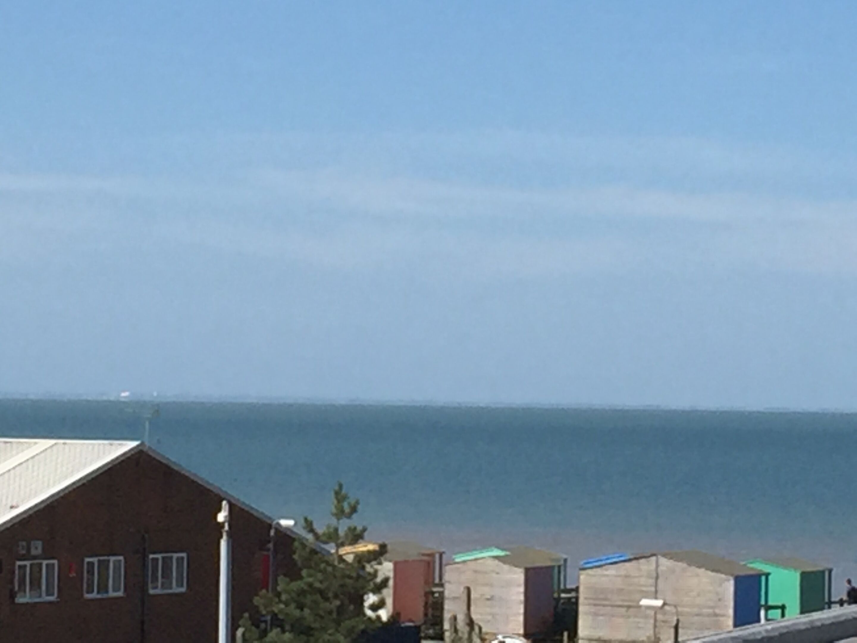 A coastal building with a flat roof, adjacent to a row of colorful beach huts.