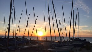 A marina with multiple sailboats docked, a sunset in the background, and a clear sky.