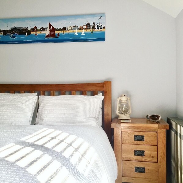 A bedroom with a bed, a nightstand, a lamp, and a painting of a coastal scene.