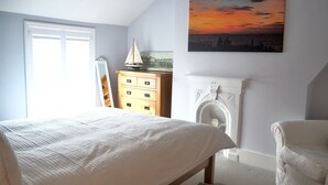 A bedroom with a bed, dresser, chair, and a painting of a sunset.