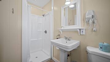 Baño con ducha, lavamanos, inodoro y secador de pelo fijado a la pared.