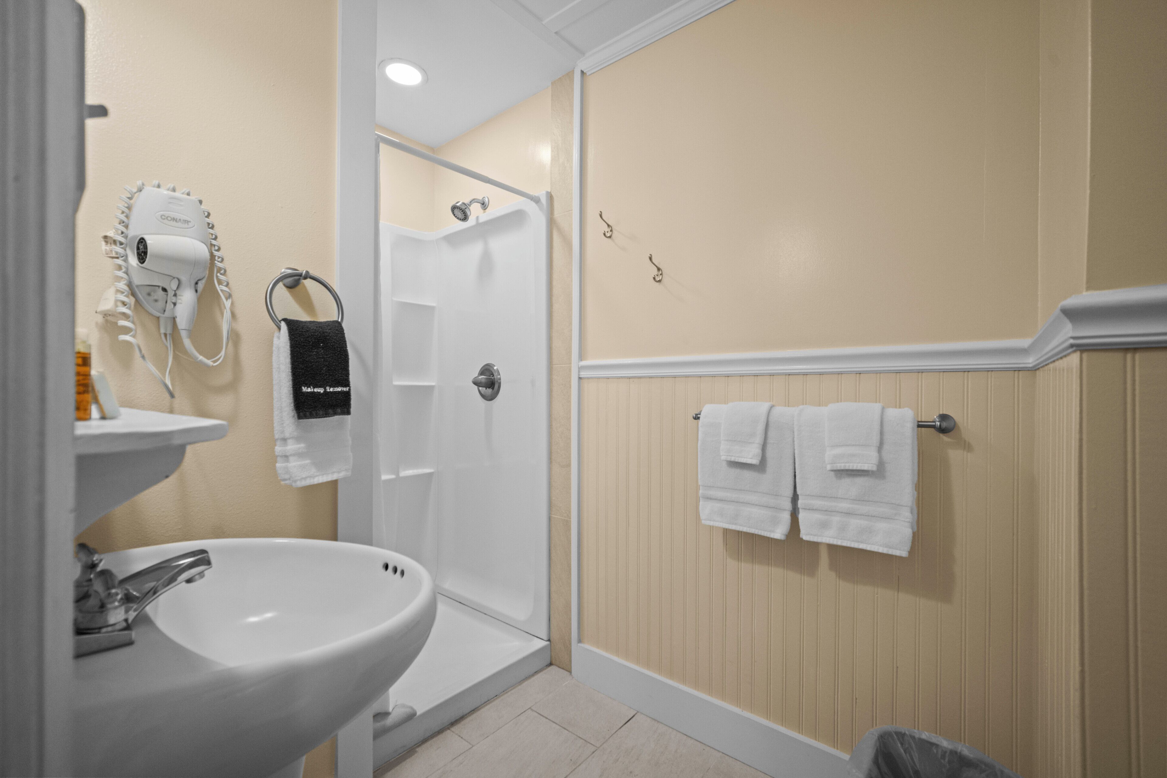 A bathroom with a sink, a hairdryer, a shower, and towels on a rack.