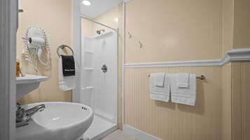 A bathroom with a sink, a hairdryer, a shower, and towels on a rack.