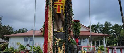 A statue of a figure adorned with garlands and flowers, surrounded by tropical plants.