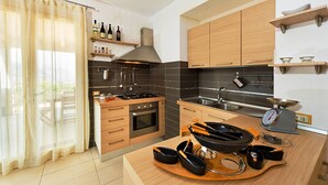 A modern kitchen with wooden cabinets, a gas stove, and a built-in oven. There are wine bottles on a shelf above the stove and a scale on the counter.