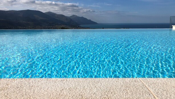 A clear blue pool with a view of mountains and the ocean.