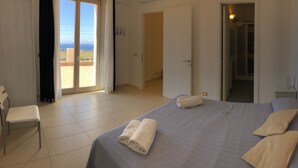 A hotel room with a bed, a chair, a bathroom, and a view of the sea.