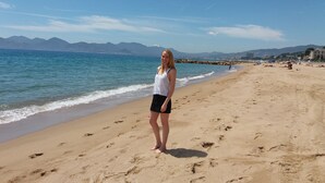 Una playa con una persona de pie sobre la arena, montañas al fondo y un cielo despejado.