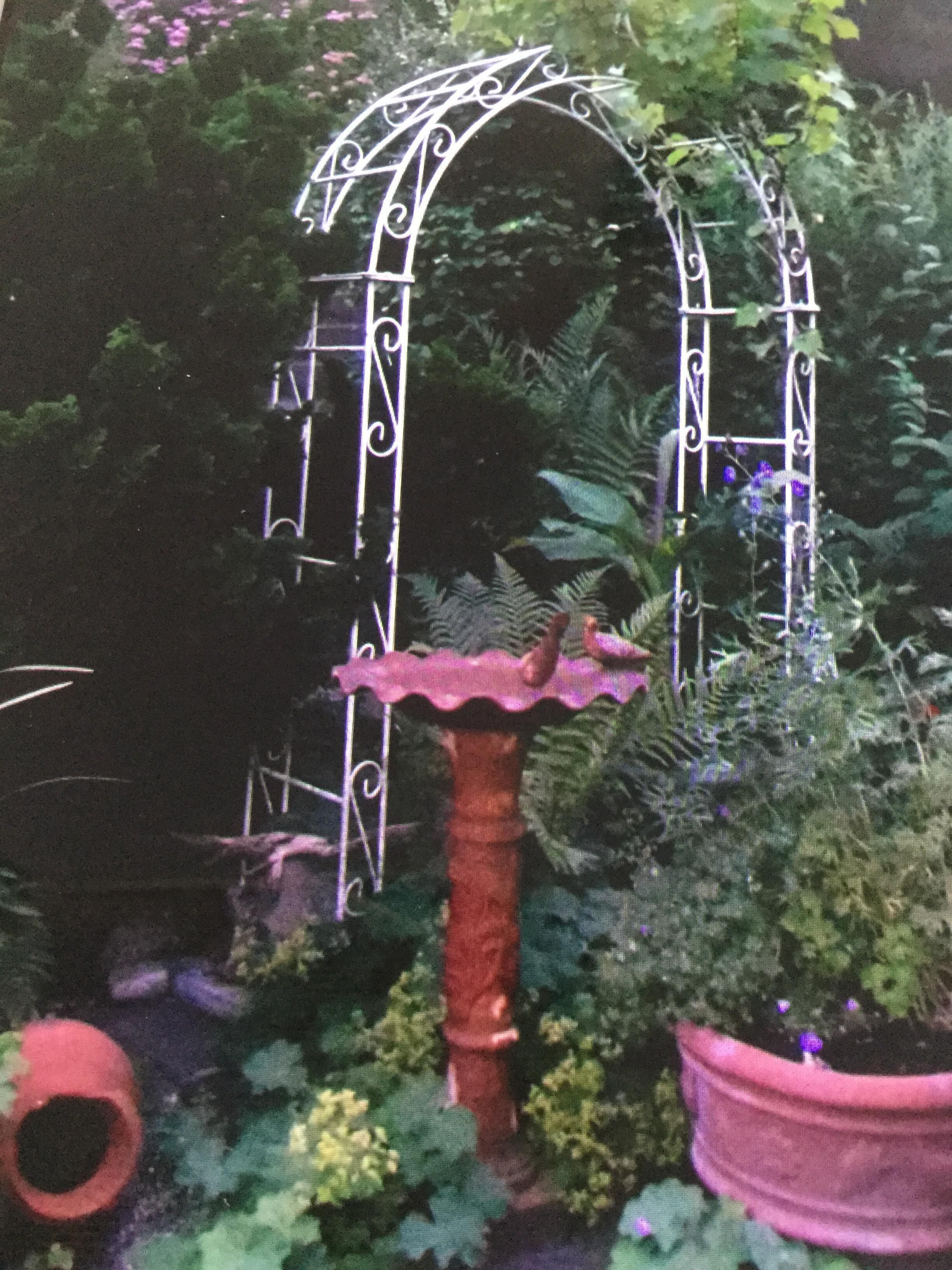 Ein Garten mit einem schmiedeeisernen Bogen und einem rosa Pflanzkasten.