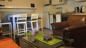 Un salon avec une table basse en verre, un canapé en cuir marron et un coin repas comprenant des chaises blanches et une petite table.