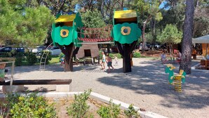 A playground with two large tree-shaped play structures, a wooden bench, and a small garden area.