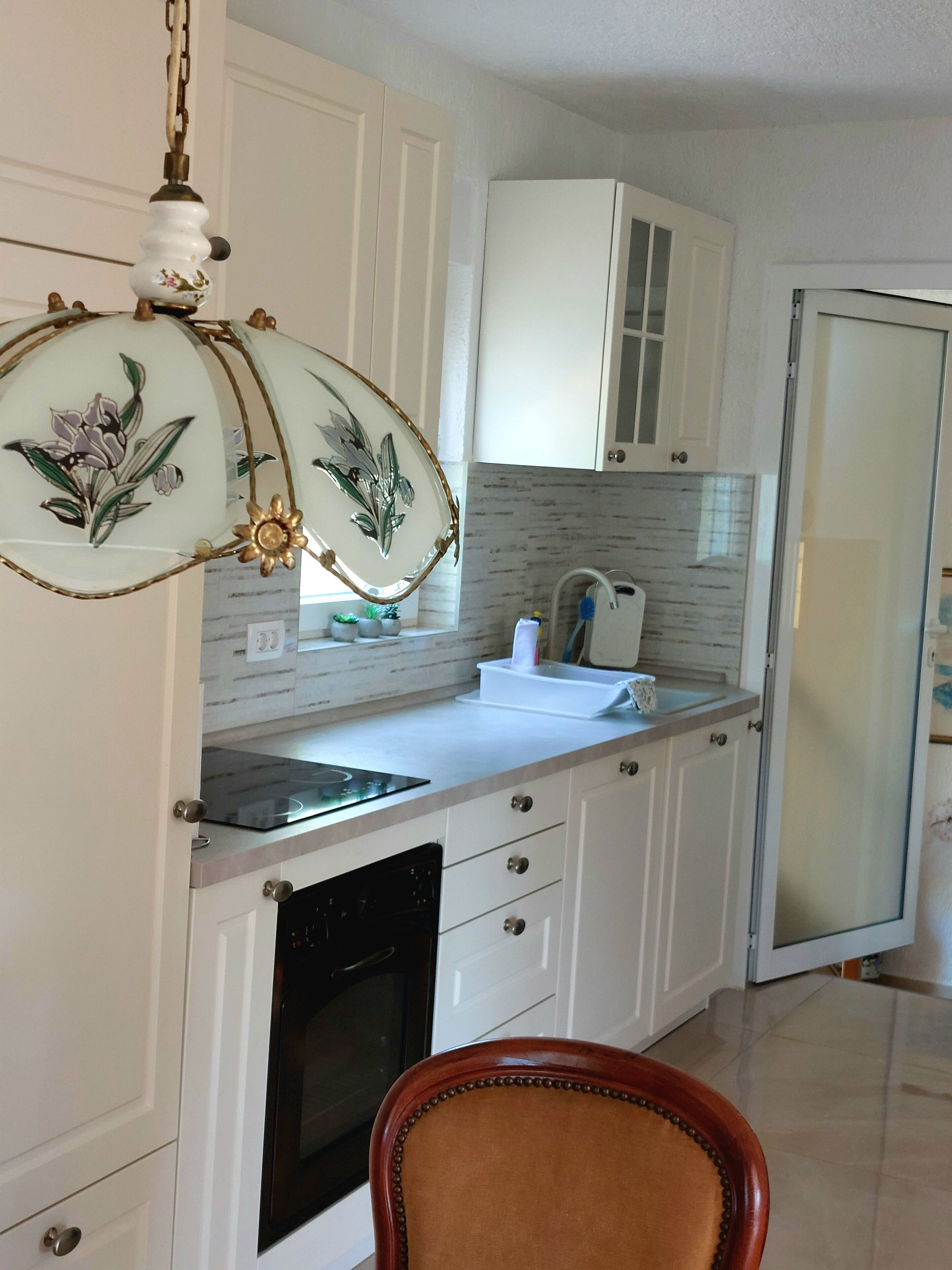 A kitchen with white cabinets, a built-in oven, a sink, and a decorative light fixture.