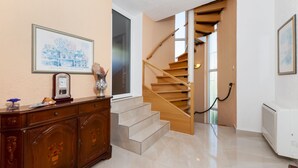 A staircase leading to a second floor, a wooden cabinet with a clock, and a framed picture on the wall.