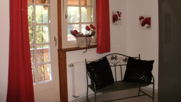 Una habitación con un banco, una ventana con cortinas rojas y un radiador.