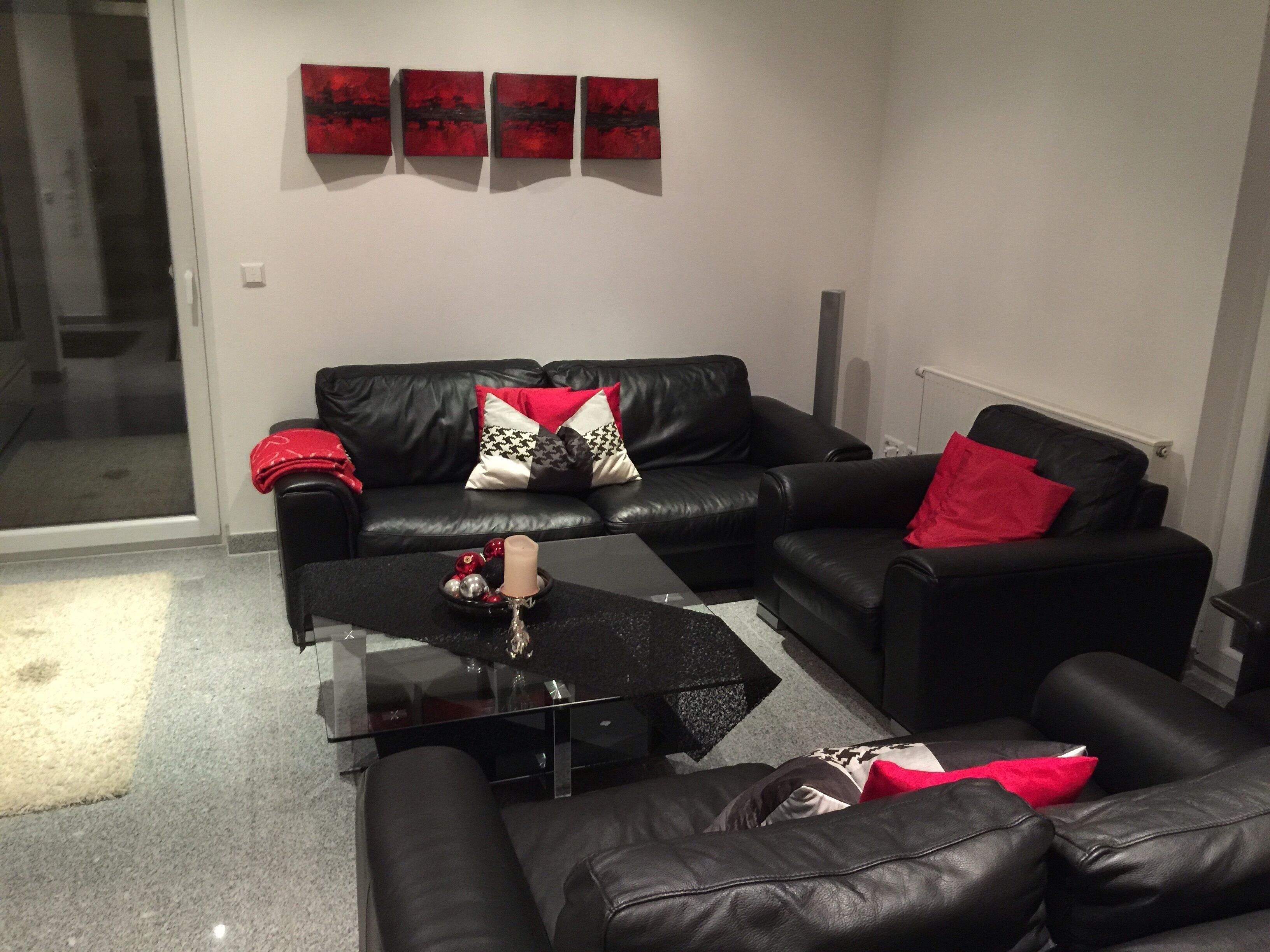 A modern living room with a black leather sofa, a glass coffee table, and a red and white patterned throw pillow.