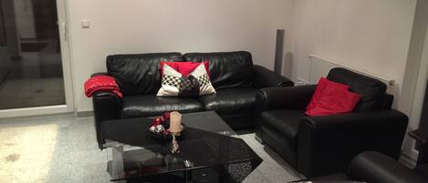 A modern living room with a black leather sofa, a glass coffee table, and a red and white patterned throw pillow.