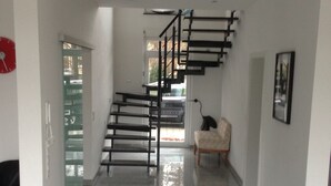 Un interior moderno con una escalera, una puerta de cristal, un tapete blanco y negro y una silla.
