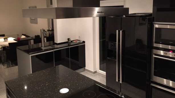 Una cocina moderna con encimera negra, electrodomésticos de acero inoxidable y horno empotrado.