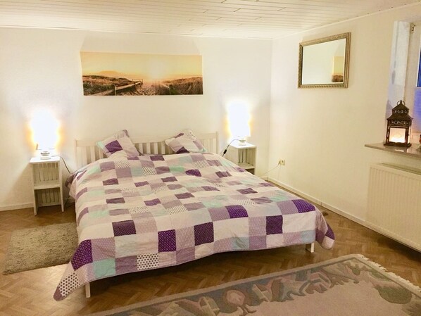 A bedroom with a bed, two bedside lamps, a nightstand, a painting on the wall, a mirror, and a small table with a lantern. - Apartment in the romantic garden<br>Note days of action !!! (Amelinghausen)
