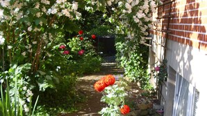A brick pathway leading through a garden with white and red flowers, surrounded by greenery and a brick building. - Apartment in the romantic garden<br>Note days of action !!!  (Amelinghausen)