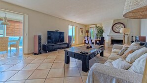 A spacious living room with a large TV, a fireplace, and a dining area with a view. - Spacious air-conditioned villa, heated pool and SPA, breathtaking views. (Grasse)