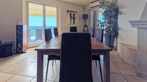 A dining area with a wooden table and chairs, a large potted plant, and a painting on the wall. - Spacious air-conditioned villa, heated pool and SPA, breathtaking views. (Grasse)